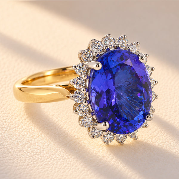 Three-quarter view of a 5.18ct oval blue-violet tanzanite ring with diamond halo and 18ct yellow gold split shoulders, showing the gemstone setting.
