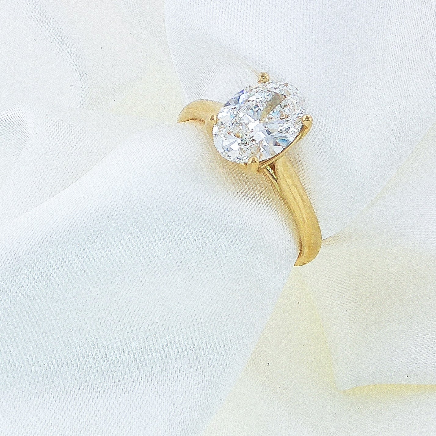 Oval Diamond Solitaire Engagement Ring in yellow gold on a white fabric background
