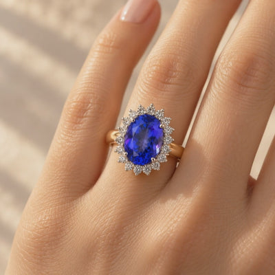 Close-up video of a 5.18ct oval blue-violet tanzanite and diamond halo ring worn on a woman's hand, showcasing its 18ct yellow gold band and sparkling diamonds.